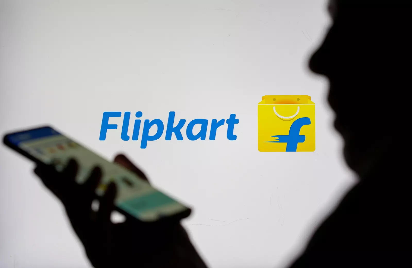 Woman with smartphone is seen in front of displayed Flipkart logo in this illustration taken